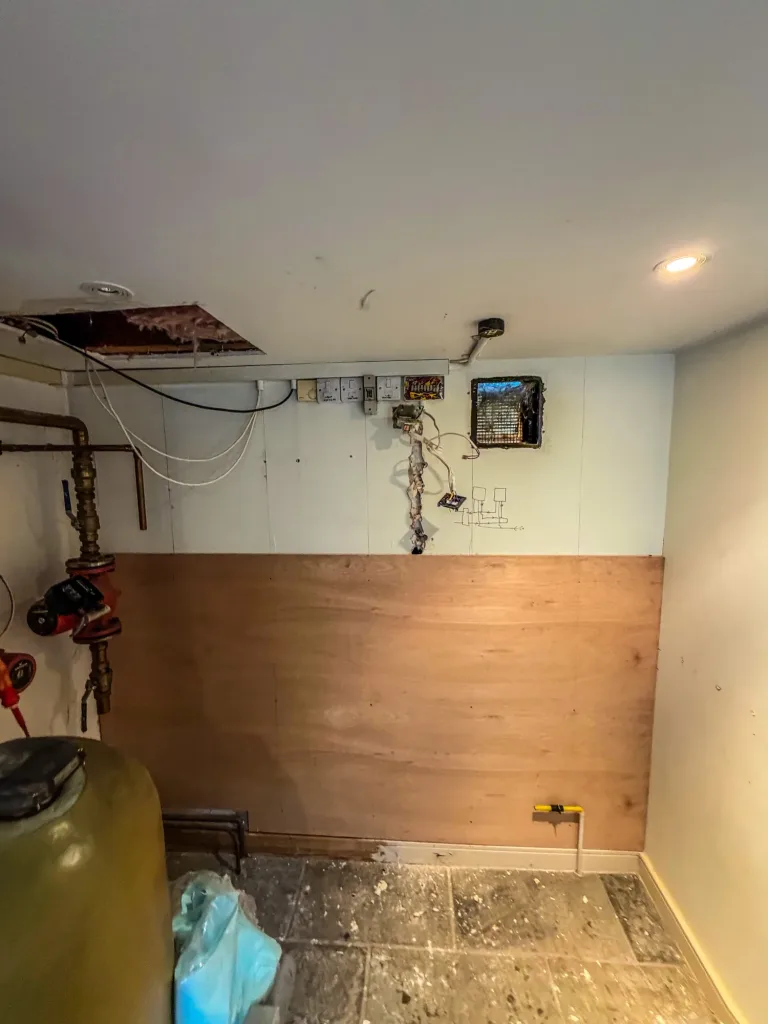 The plant cupboard stripped out after the old boiler was removed, with a plywood mounting board fitted and the gas supply capped ready for the new boilers