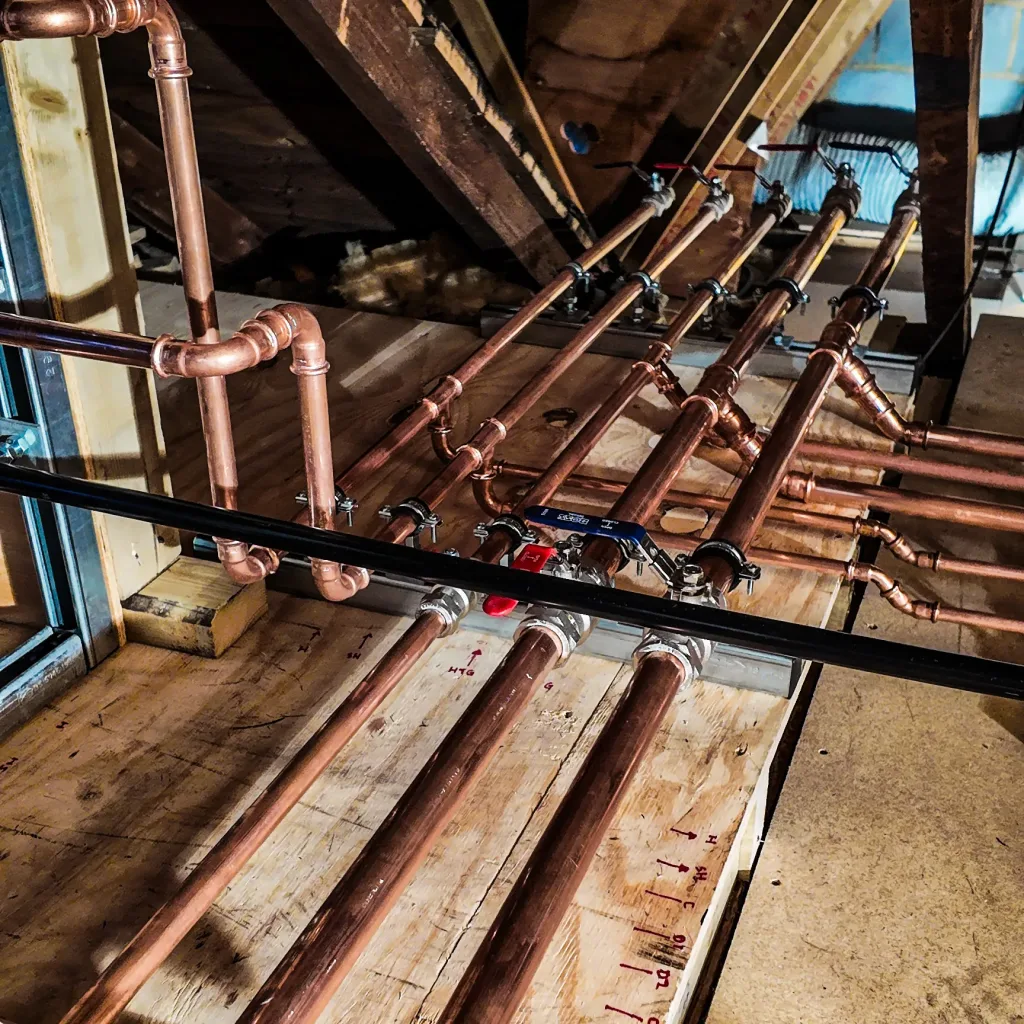 New hot and cold water distribution pipework running through the loft with isolation valves and labelled service runs