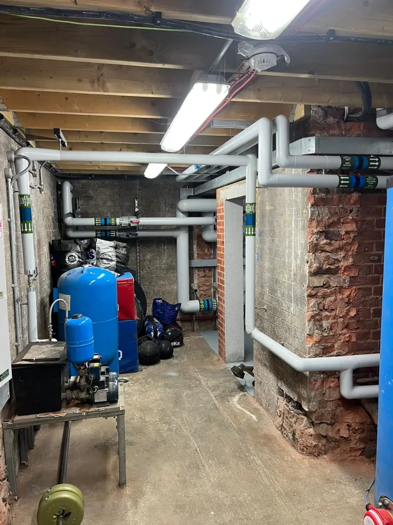 Blue expansion vessel and pressurisation unit mounted on a stand with overhead insulated distribution pipework.