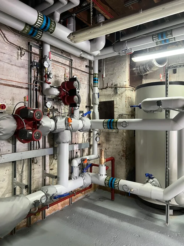 Twin red circulating pumps mounted on insulated heating distribution pipework with dial pressure gauges and valves.