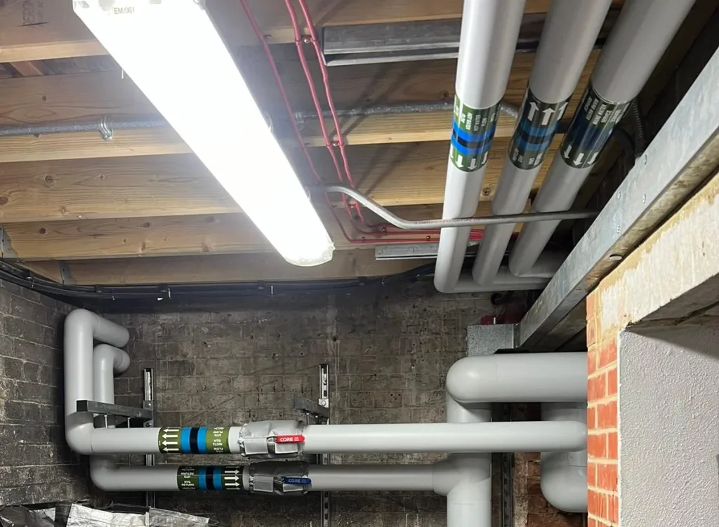 Insulated heating and hot water distribution pipes with identification banding suspended below timber floor joists.