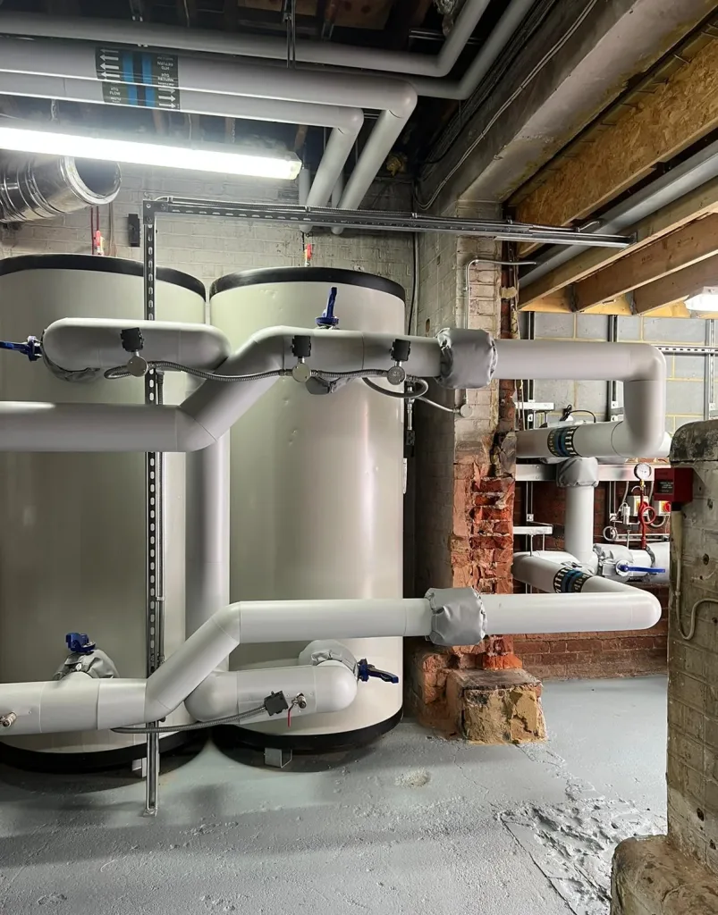 Two large vertical insulated buffer vessels connected to horizontal flow and return pipework on steel frames.