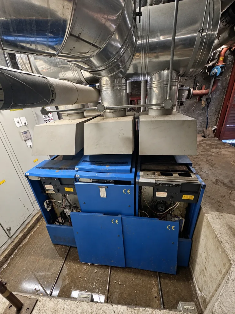 The three original floor-standing gas boilers before removal, with casing panels open and flue hoods above