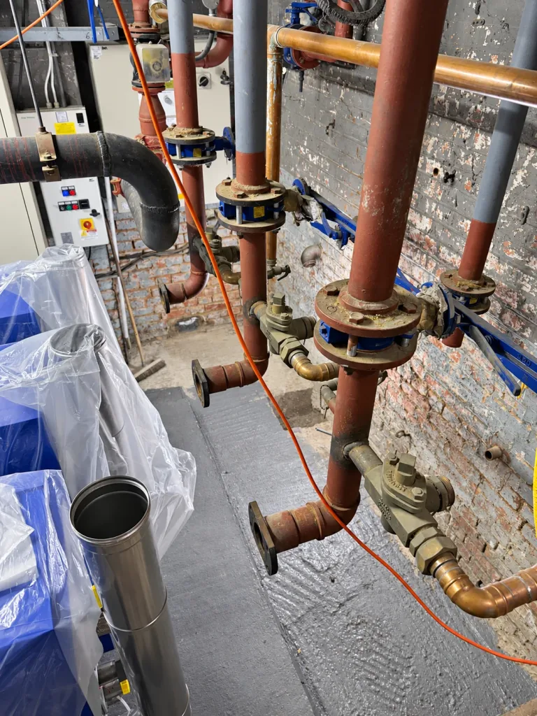 Plant room during strip-out, with capped pipework branches and equipment protected under sheeting