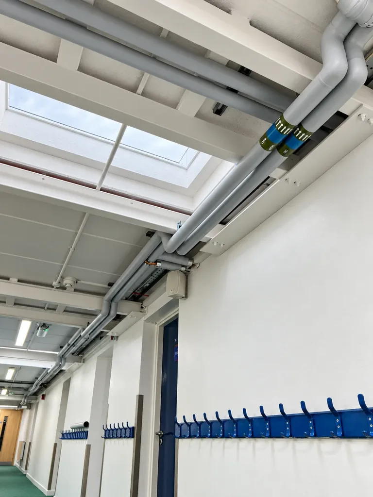 LTHW flow and return pipework with identification banding running at high level beneath a corridor rooflight