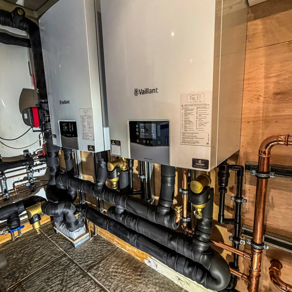 Angled view of the completed twin Vaillant boiler installation, with insulated primary pipework, isolation valves and a Grundfos circulator to the left
