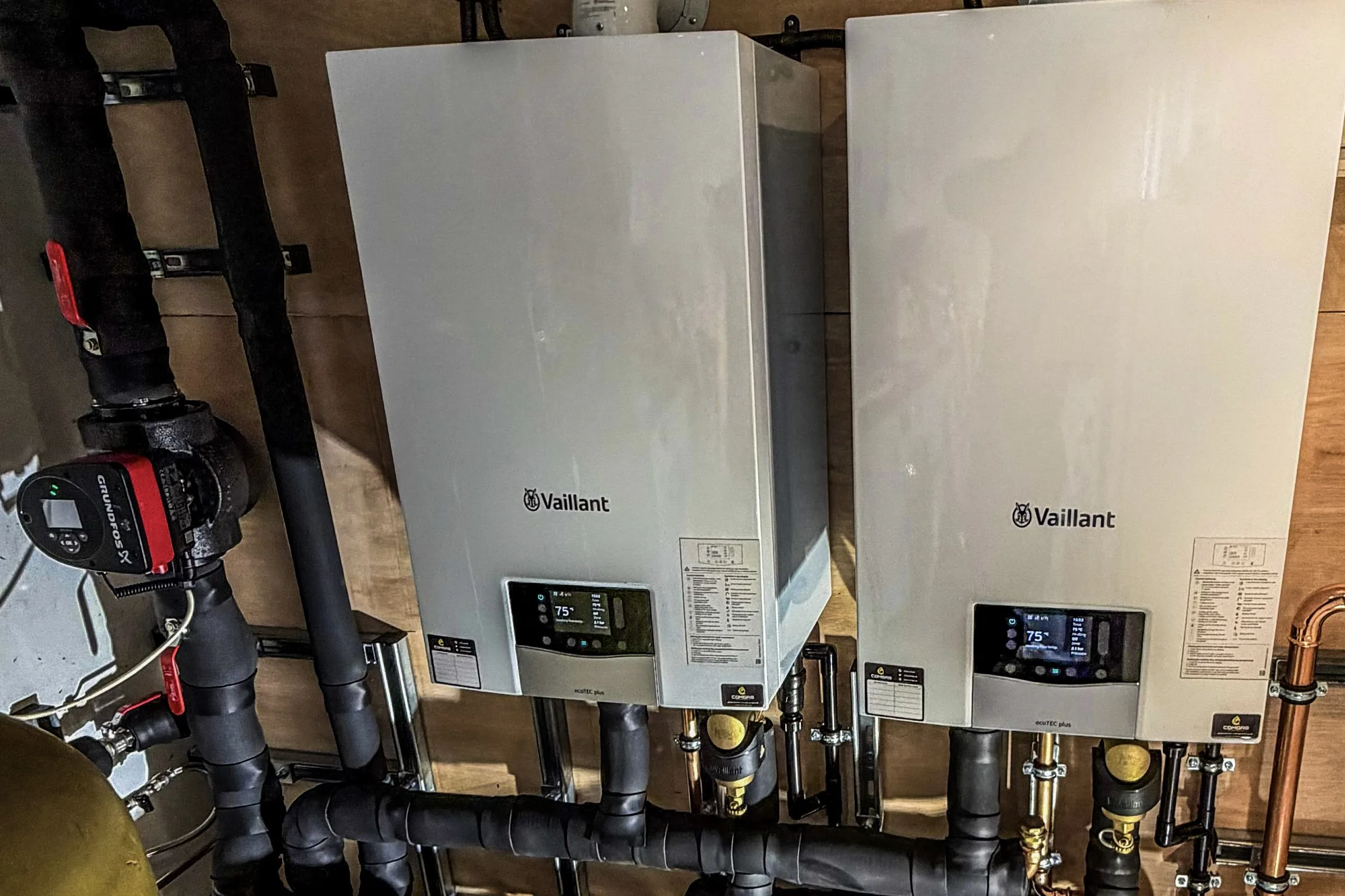 Two Vaillant ecoTEC plus boilers mounted side by side in a domestic plant cupboard, with black-insulated primary pipework running below them