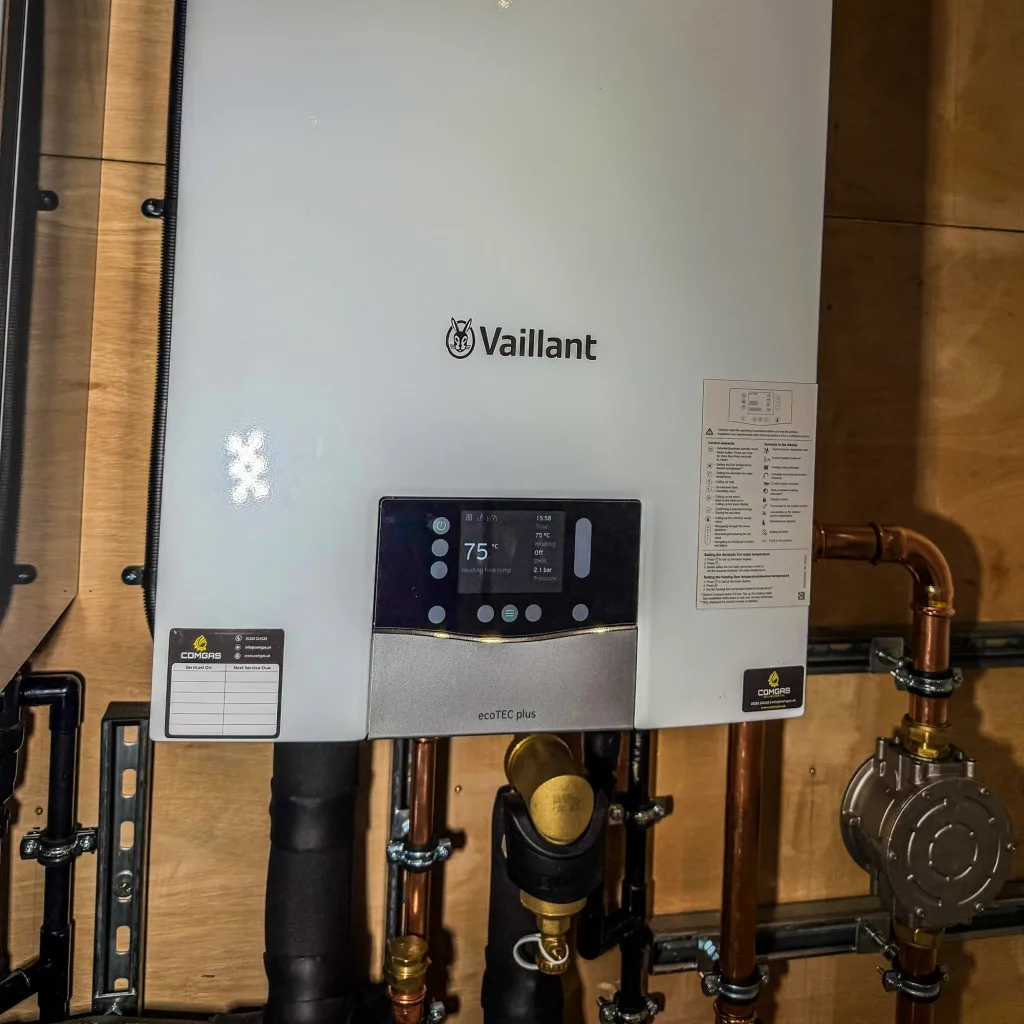 Close-up of a wall-mounted Vaillant ecoTEC plus boiler reading 75 degrees and 2.1 bar, with a blank ComGas service record sticker on the casing